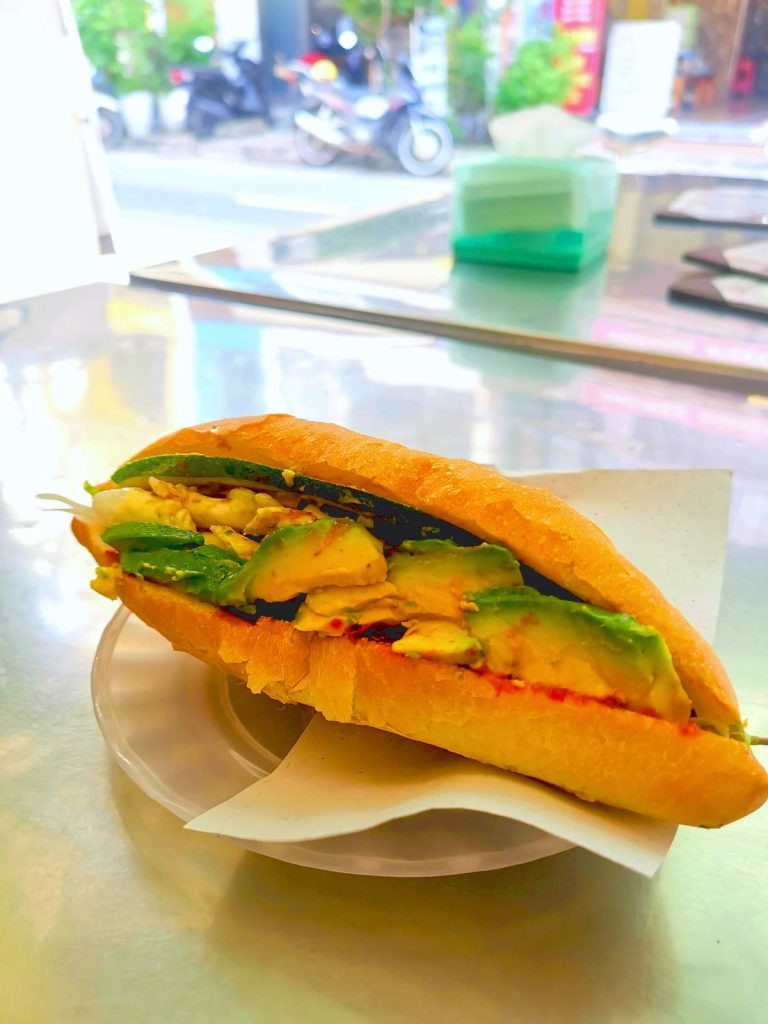 Bánh mì Hội An kẹp bơ tươi ngon, một lựa chọn phổ biến tại Phi Bánh Mì, trên bàn kim loại đơn giản.