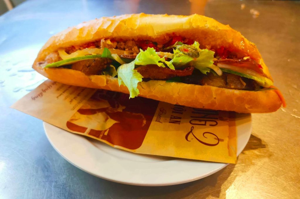 Bánh mì Hội An nhân thịt, pa tê và rau xà lách tươi ngon trên đĩa trắng, gợi nhớ đến món ăn được Anthony Bourdain ca ngợi.