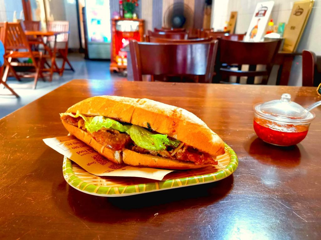 Chiếc bánh mì Hội An truyền thống nóng giòn, đầy đặn nhân, được phục vụ trên đĩa tại Bánh Mì Sùm, một địa điểm nổi bật.