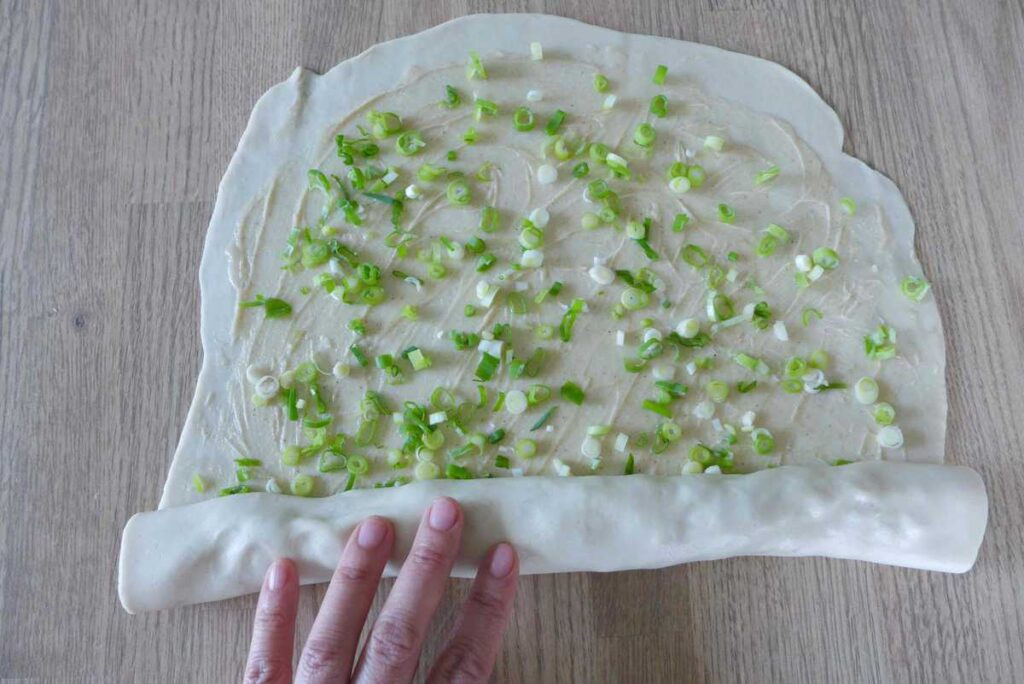 Cuộn miếng bột đã phết nhân hành lá để tạo hình bánh hành chiên