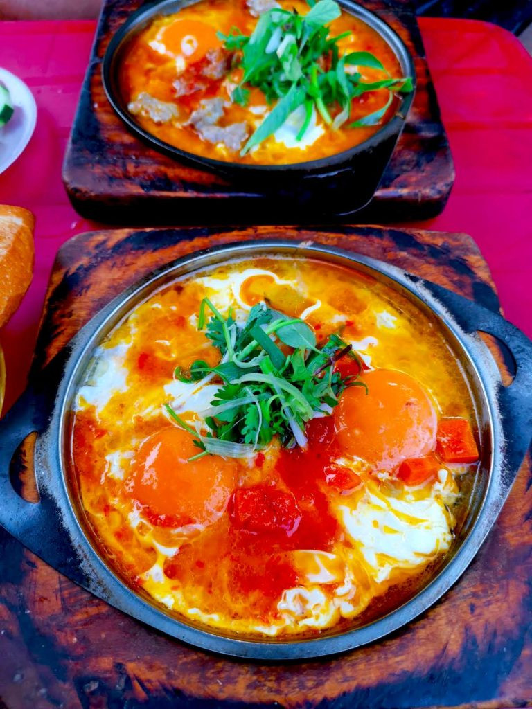 Hai đĩa ốp la nóng hổi với trứng ốp la, cà chua và rau thơm, sẵn sàng để làm nên những chiếc bánh mì Hội An cho bữa sáng tại Op La Đồng.