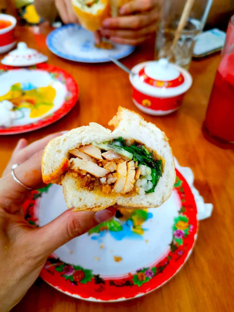 Thực khách đang cầm chiếc bánh mì Hội An đầy ắp thịt và rau tại tiệm Madam Khanh, Bánh Mì Nữ Hoàng nổi tiếng.