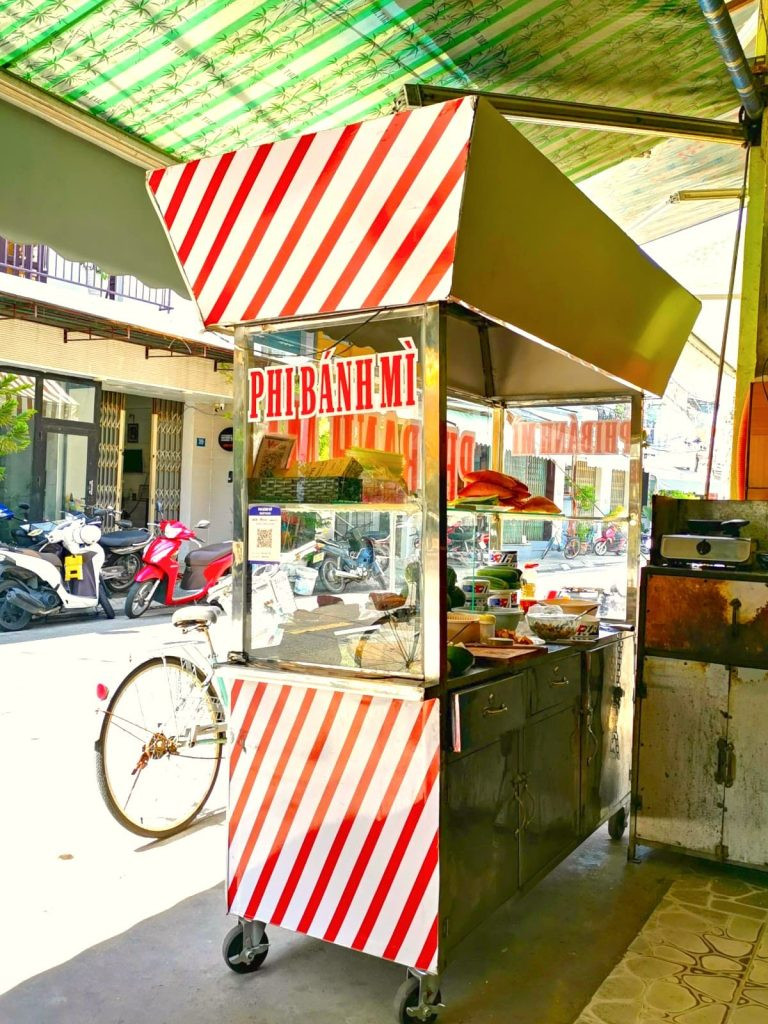 Xe bánh mì Phi Bánh Mì Hội An với mái che sọc đỏ trắng đặc trưng, thu hút du khách bởi hương vị truyền thống.