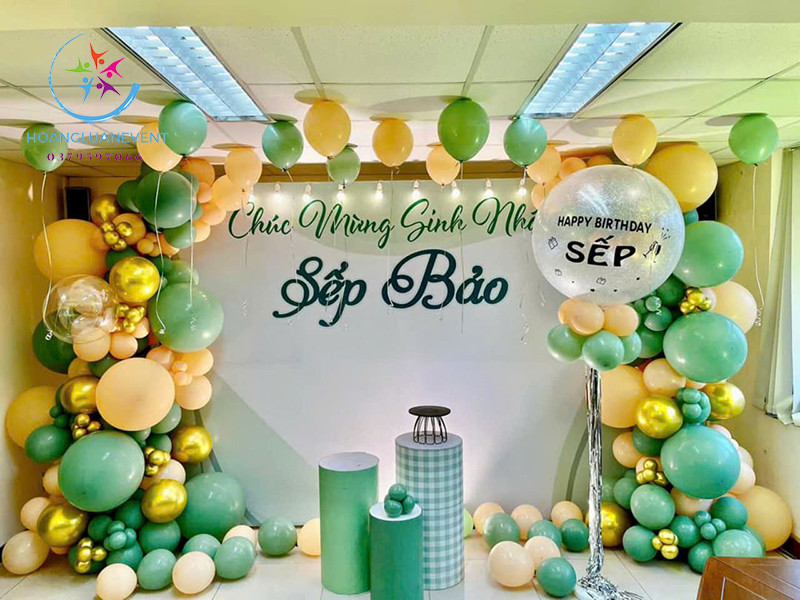 Hình ảnh một bữa tiệc sinh nhật người lớn với phông nền vàng đồng sang trọng, chữ 'Happy Birthday' lớn và bóng bay lấp lánh, phù hợp cho không gian tiệc ấm cúng.