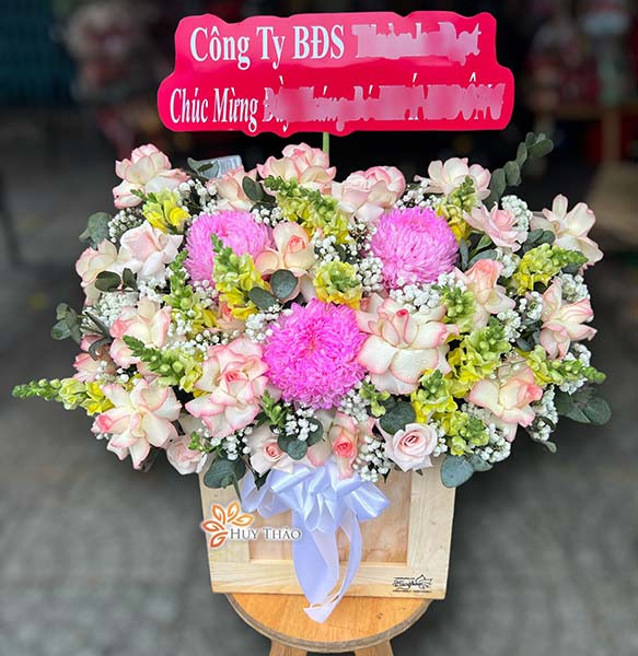 Lẵng hoa chúc mừng sinh nhật màu hồng phấn rực rỡ, trang trí với hoa hồng, lan và lá xanh tươi tắn, biểu tượng cho sự may mắn và hạnh phúc.