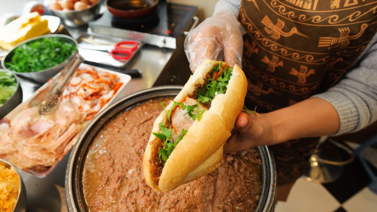 Một chiếc bánh mì kẹp giòn rụm với đầy đủ các loại nhân như thịt nguội, pate và dưa chua, minh họa món ăn Việt Nam.